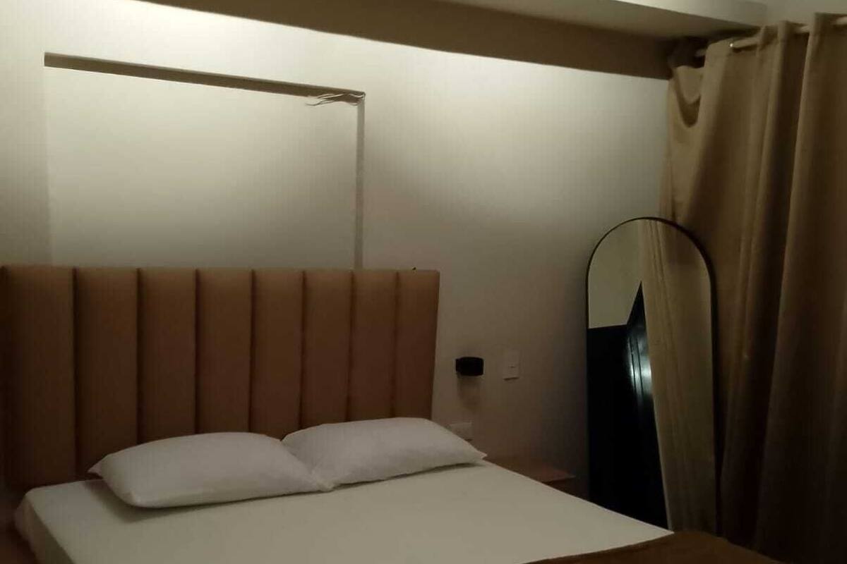 Ein Hotelzimmer mit Bett, Nachttisch, Lampe, Spiegel und Vorhängen.