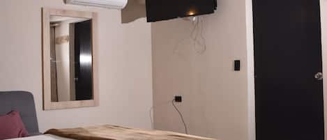 Een slaapkamer met een bed, een wandtelevisie, een airconditioningsunit en een deur.
