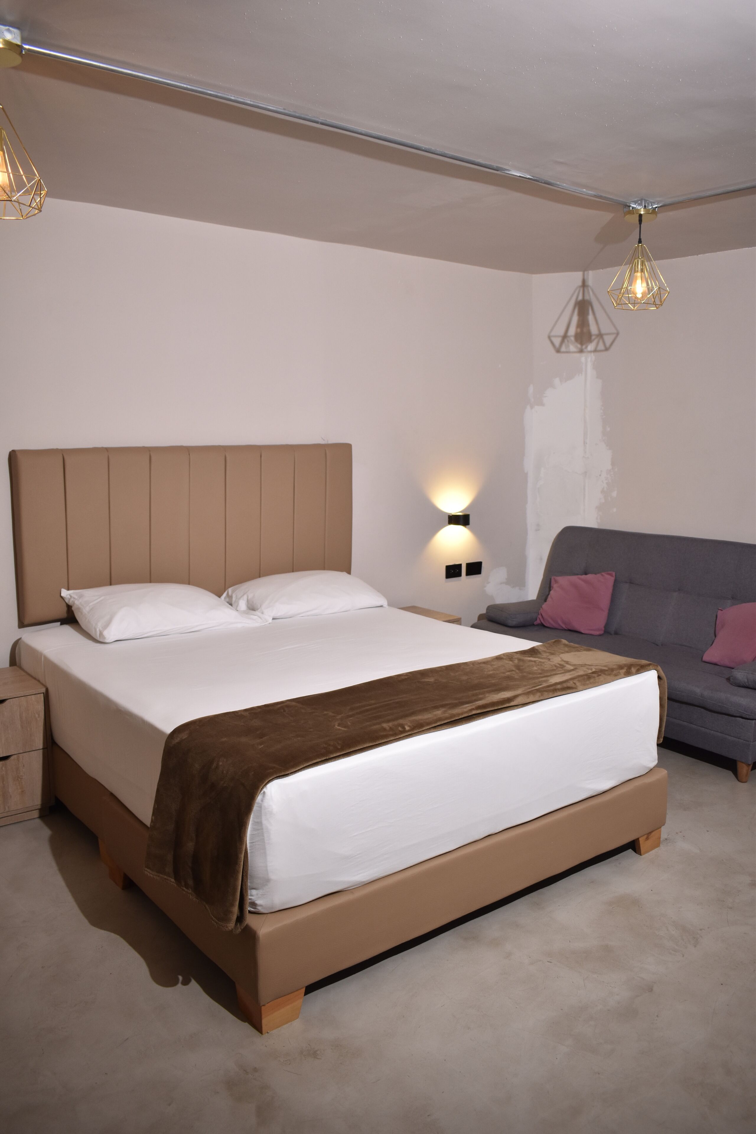 A bedroom with a large bed, a nightstand, a sofa, and a wall-mounted light fixture.