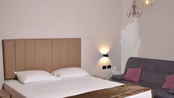 A bedroom with a large bed, a nightstand, a sofa, and a wall-mounted light fixture.