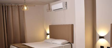 A hotel room with two beds, a ceiling fan, and a wall-mounted air conditioner.