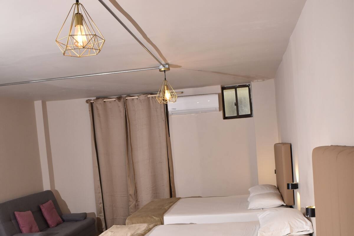 Ein Hotelzimmer mit drei Betten, einer Couch und einer modernen Pendelleuchte.