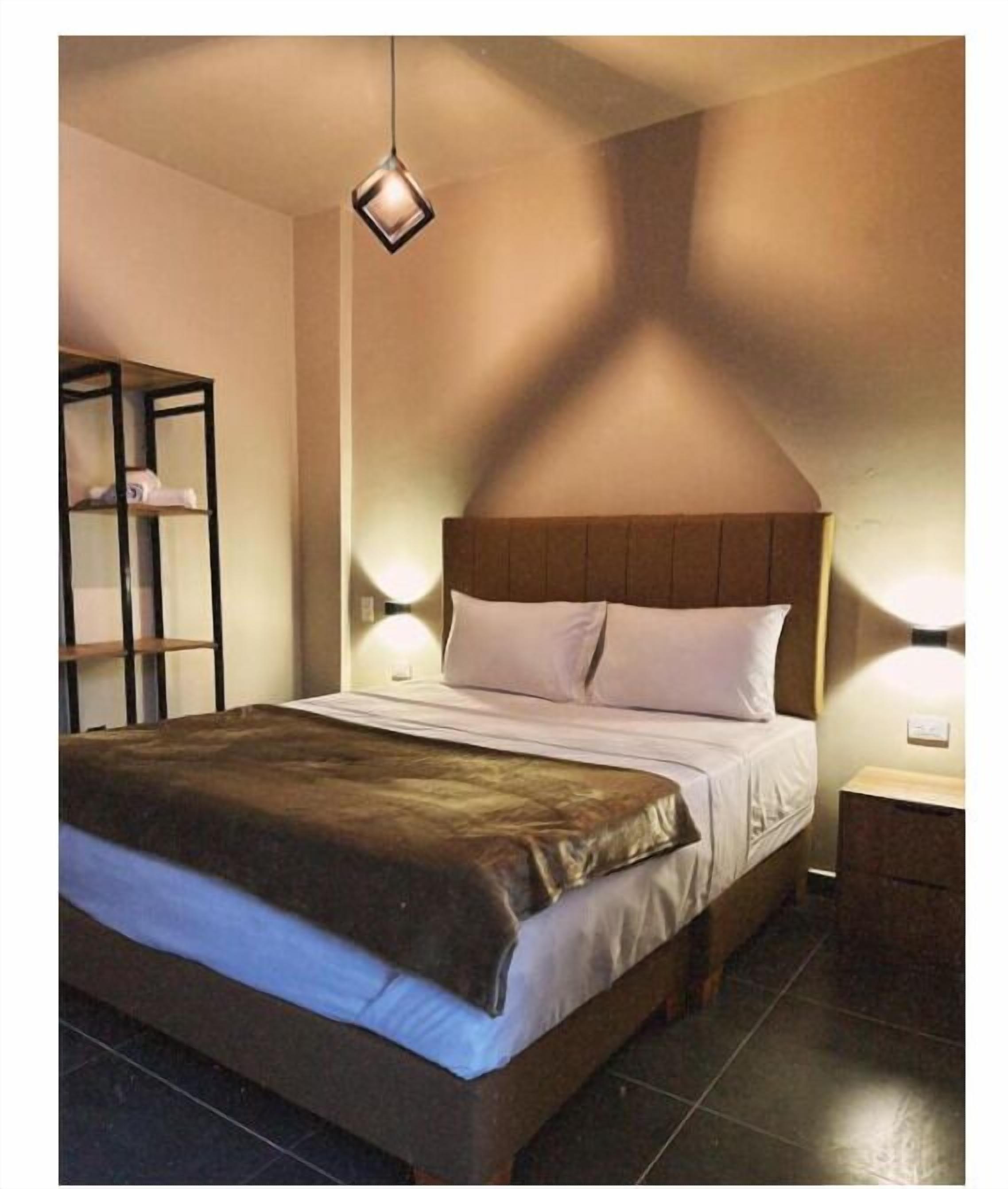 A bedroom with a large bed, a wooden headboard, a nightstand, and a wall-mounted shelf.