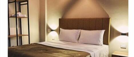 A bedroom with a large bed, a wooden headboard, a nightstand, and a wall-mounted shelf.