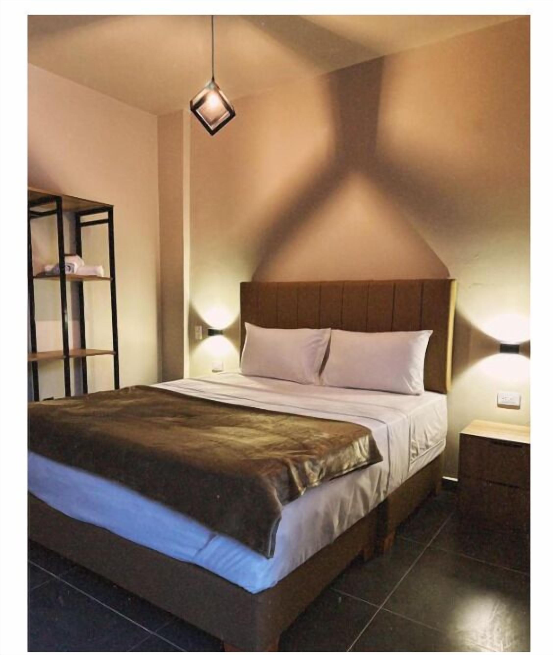 Un dormitorio con cama, mesita de noche, estante y lámpara colgante.