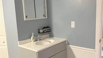 Een badkamer met een witte wastafel, een spiegel, een wasbak en een prullenbak.