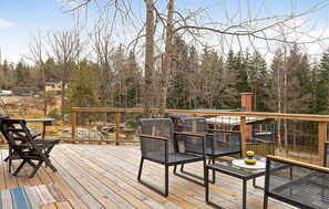 Um deck de madeira com móveis de exterior, incluindo cadeiras e uma mesa, com vista para uma área arborizada.