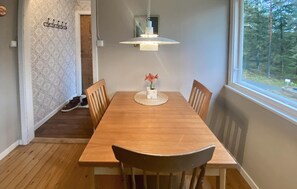 Uma sala de jantar com uma mesa de madeira, cadeiras, um lustre e uma janela com vista para árvores.