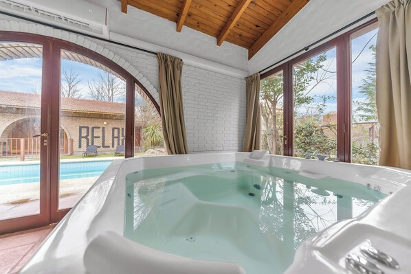 Une salle de spa dotée d’un bain à remous, de grandes fenêtres et offrant une vue sur une piscine et un bâtiment.