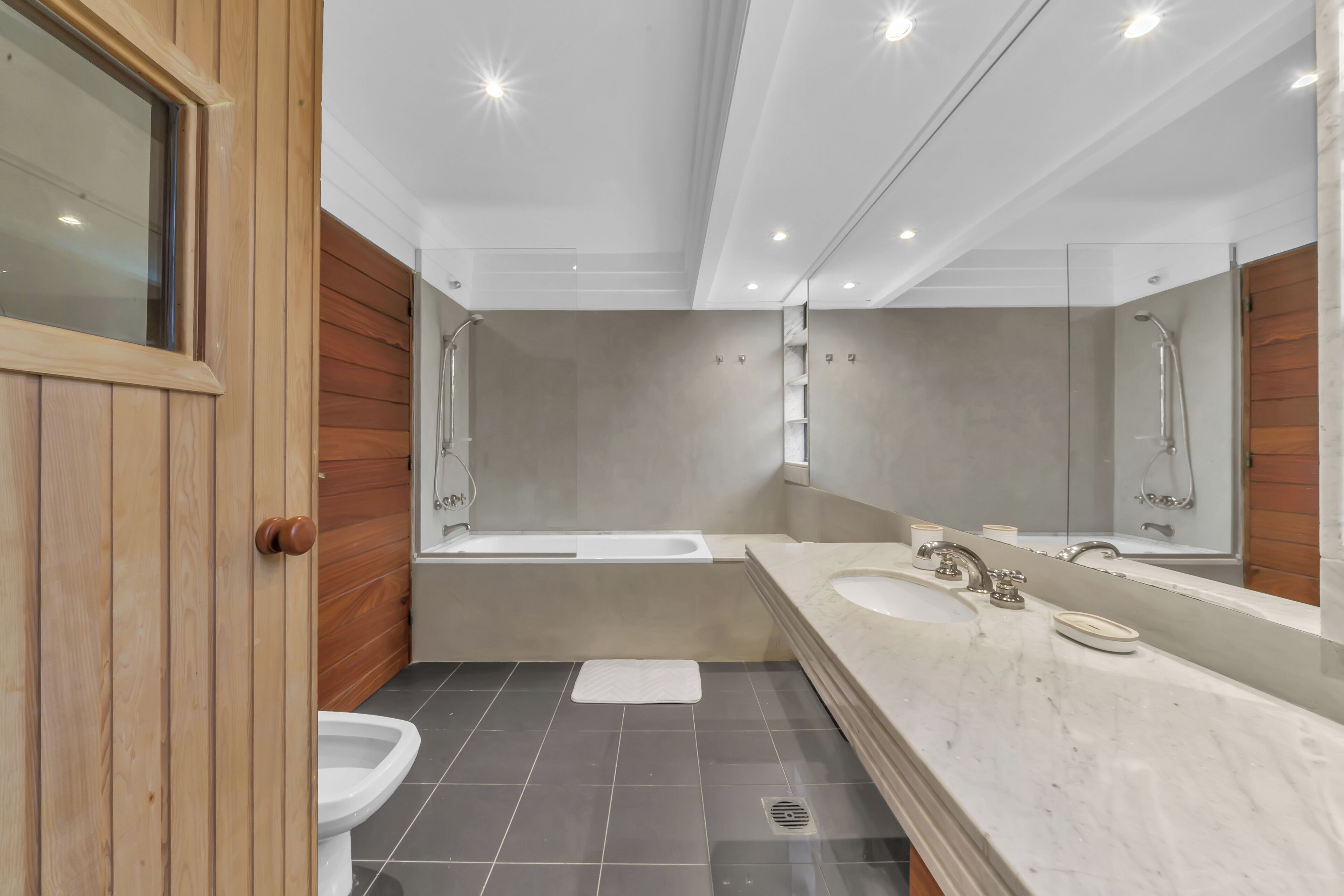 Un baño moderno con puerta de madera, una bañera, ducha y un espejo grande.