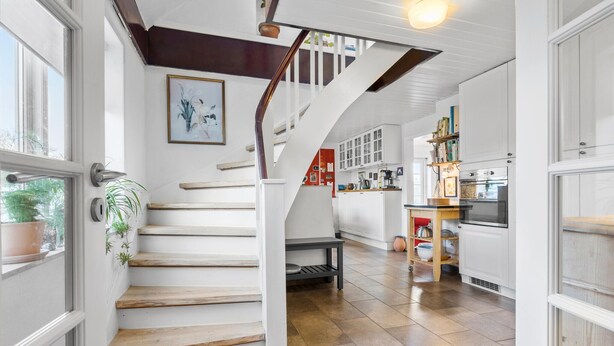 A staircase leading to a kitchen with white cabinets, a wooden table, and a potted plant. - Nice home in Farsø with WiFi (Farsø)