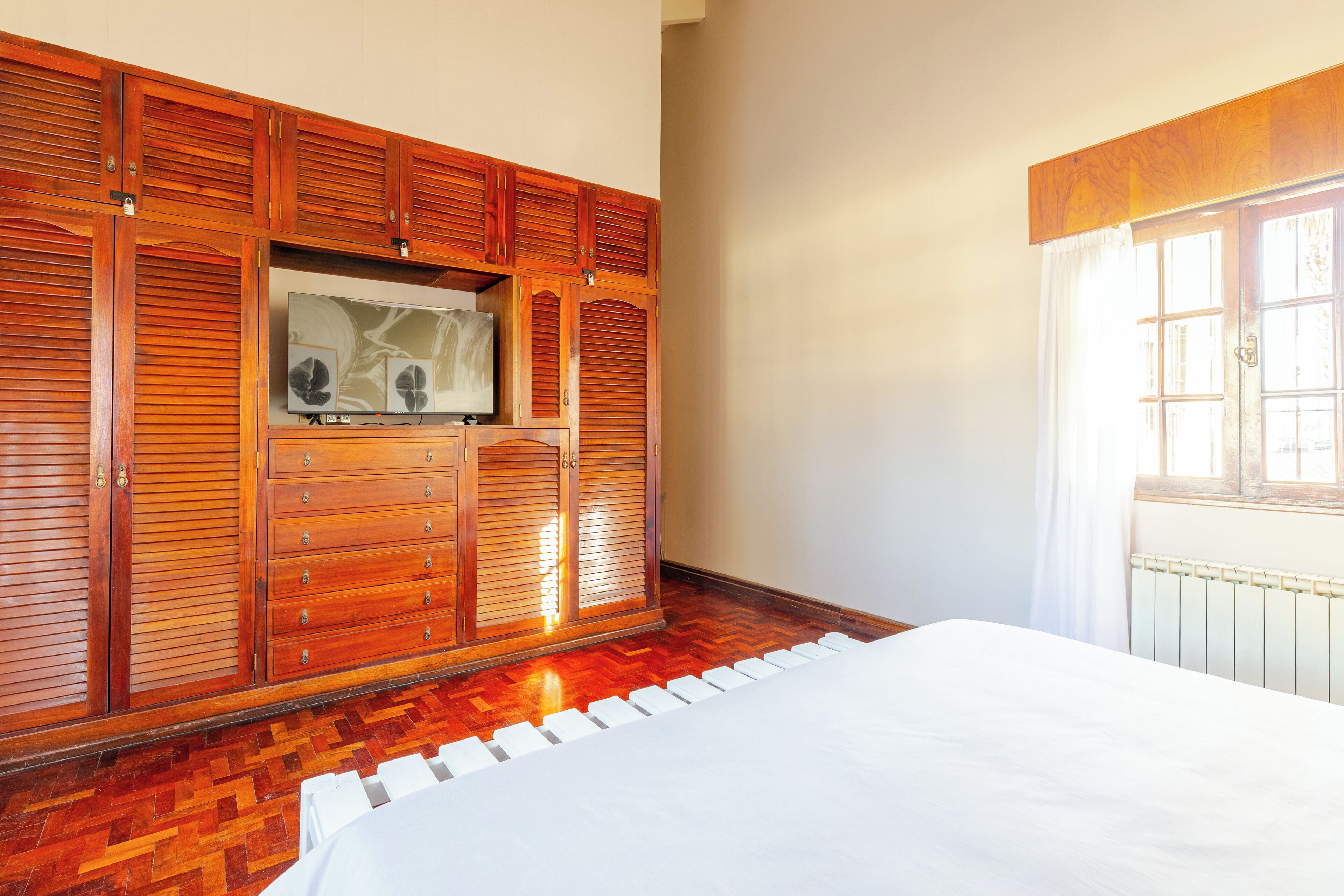 A bedroom with a large wooden wardrobe, a bed, and a radiator.