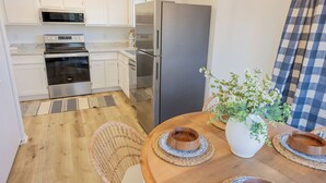 Une cuisine moderne avec des meubles blancs, des appareils en acier inoxydable et une table à manger en bois, agrémentée de sets de table en fibres tressées.
