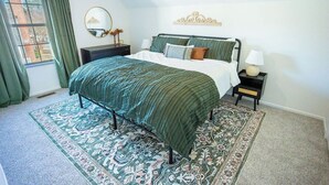 Une chambre à coucher avec un lit, une table de chevet, un miroir et une fenêtre avec des rideaux.