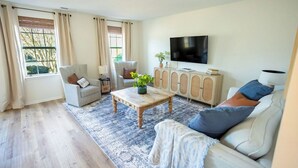 Un salon comprenant un canapé, des fauteuils, une table basse, un téléviseur et un meuble.