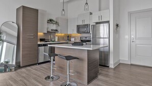 A modern kitchen with stainless steel appliances, a central island with bar stools, and pendant lighting. - Downtown High-Rise w/ City Views, Pool & Gym (Atlanta)