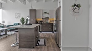 A modern kitchen with a central island, stainless steel appliances, and a hanging light fixture. - Downtown High-Rise w/ City Views, Pool & Gym (Atlanta)