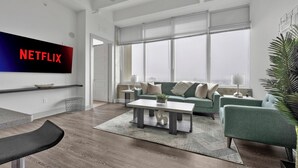 A modern living room with a large window, a green sofa, a coffee table, and a flat-screen TV mounted on the wall. - Downtown High-Rise w/ City Views, Pool & Gym (Atlanta)