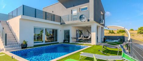 Une maison moderne à deux étages dotée d’une piscine, d’un espace salon extérieur et d’un patio couvert.