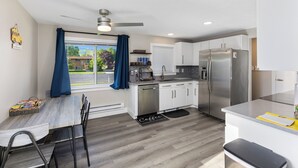 A modern kitchen with a dining area, a built-in dishwasher, a large refrigerator, and a window with blue curtains. - Cozy home in Logan, close to USU (Logan)