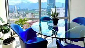 Een moderne kamer met een groot raam en uitzicht op de stad, een glazen tafel en blauwe stoelen.