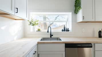 A modern kitchen with a window, a dishwasher, and white cabinetry.