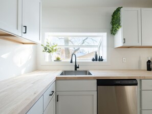 A modern kitchen with a window, a dishwasher, and white cabinetry.