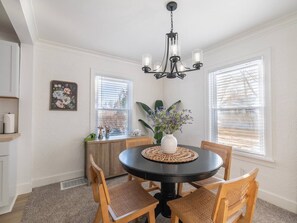 A dining area with a round table, four chairs, a vase with flowers, and a chandelier.