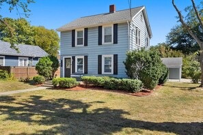 A two-story house with a front porch, a small front yard with trimmed bushes, and a garage.