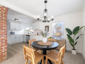 A modern kitchen with white cabinets, a dining table with chairs, and a hanging light fixture.