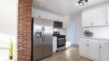 Een moderne keuken met een roestvrijstalen koelkast, magnetron en oven, witte kastjes en een accentmuur van baksteen.