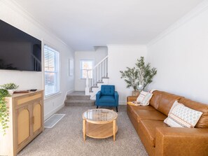 A living room with a brown leather sofa, a blue armchair, a wooden coffee table, and a television mounted on the wall.