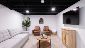 Una sala de estar moderna con un sofá gris, dos sillones de cuero, una mesa de centro de madera y un televisor montado en la pared.