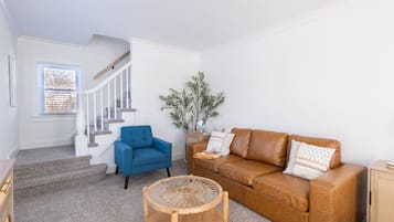 A living room with a staircase, a blue armchair, a brown sofa, and a round wooden coffee table.