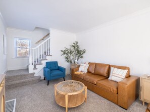 A living room with a staircase, a blue armchair, a brown sofa, and a round wooden coffee table.