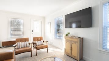 Una sala de estar con sofá, sillones, una mesa de centro y un televisor montado en la pared.