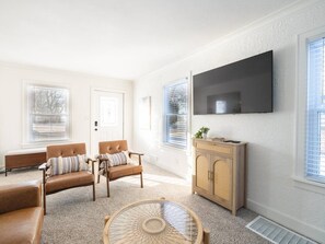 A living room with a sofa, armchairs, a coffee table, and a TV mounted on the wall.