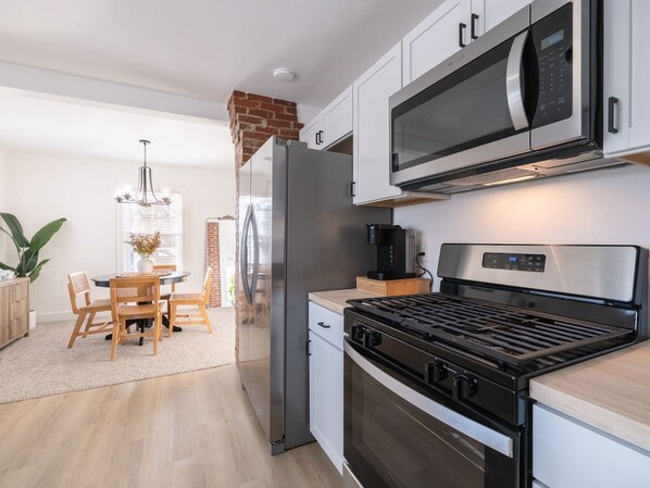 A modern kitchen with stainless steel appliances, a dining area with wooden chairs, and a brick fireplace.