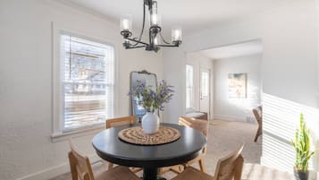 Een eetzaal met een ronde tafel, stoelen, een vaas met bloemen en een kroonluchter.