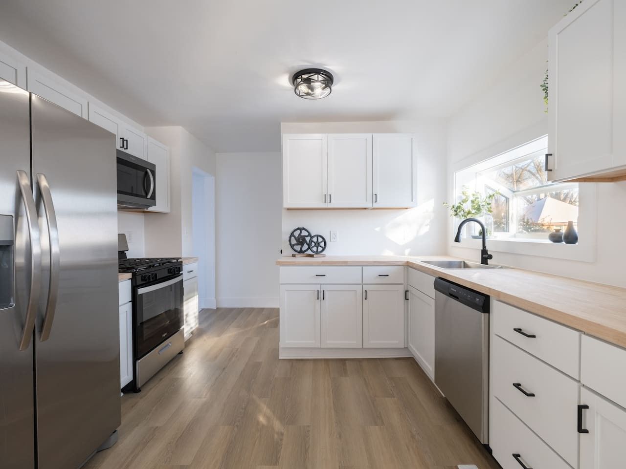 A modern kitchen with white cabinets, stainless steel appliances, and a wooden floor.