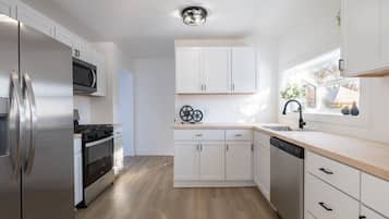 A modern kitchen with white cabinets, stainless steel appliances, and a wooden floor.