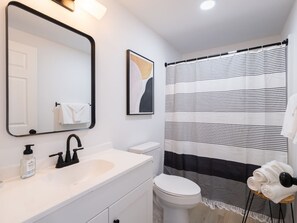 A modern bathroom with a white sink, black faucet, a toilet, and a striped shower curtain.