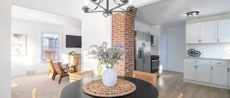 A dining area with a round table, chairs, a vase with flowers, and a brick pillar.