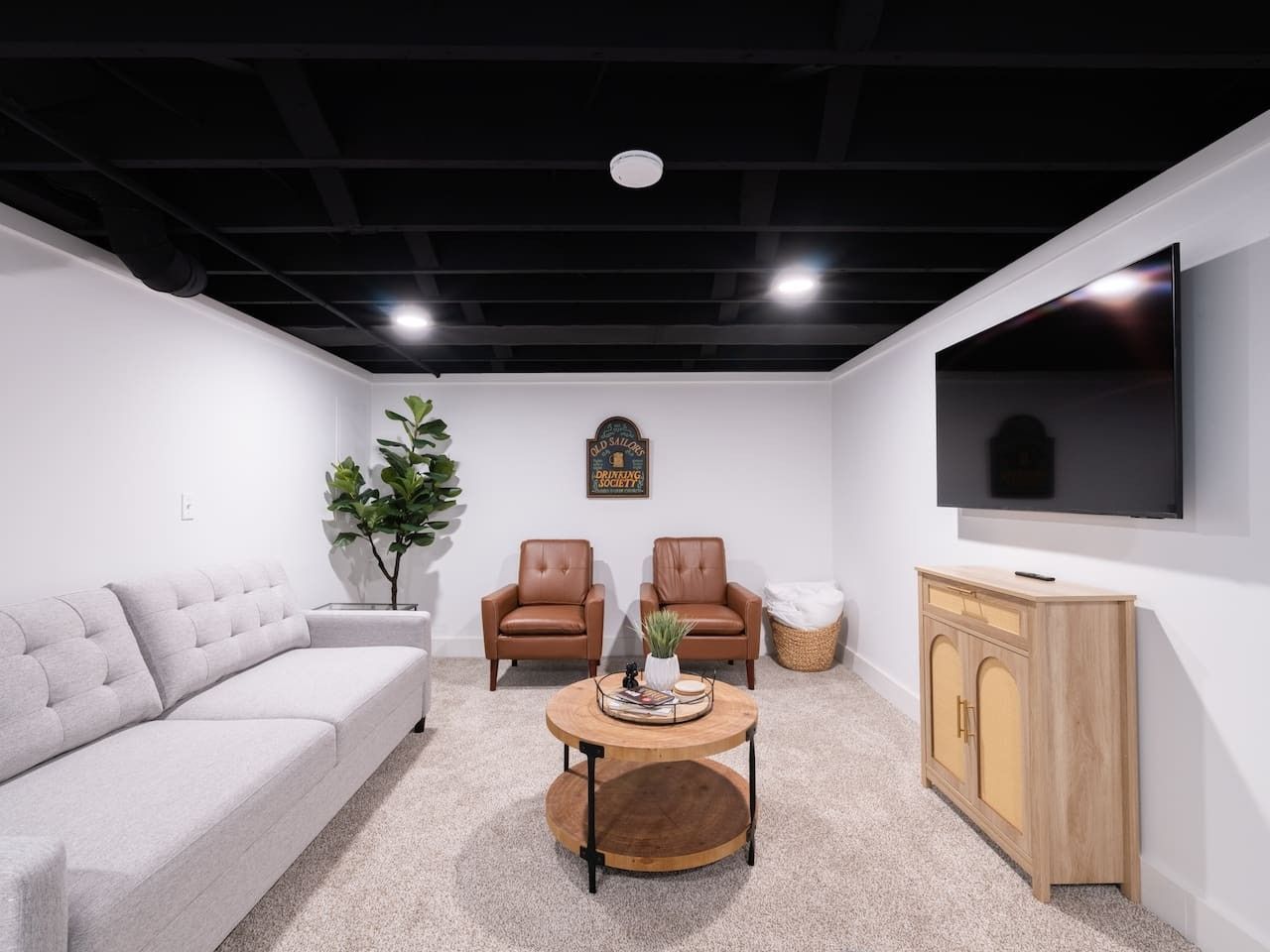 A modern living room with a sofa, two armchairs, a coffee table, and a TV mounted on the wall.