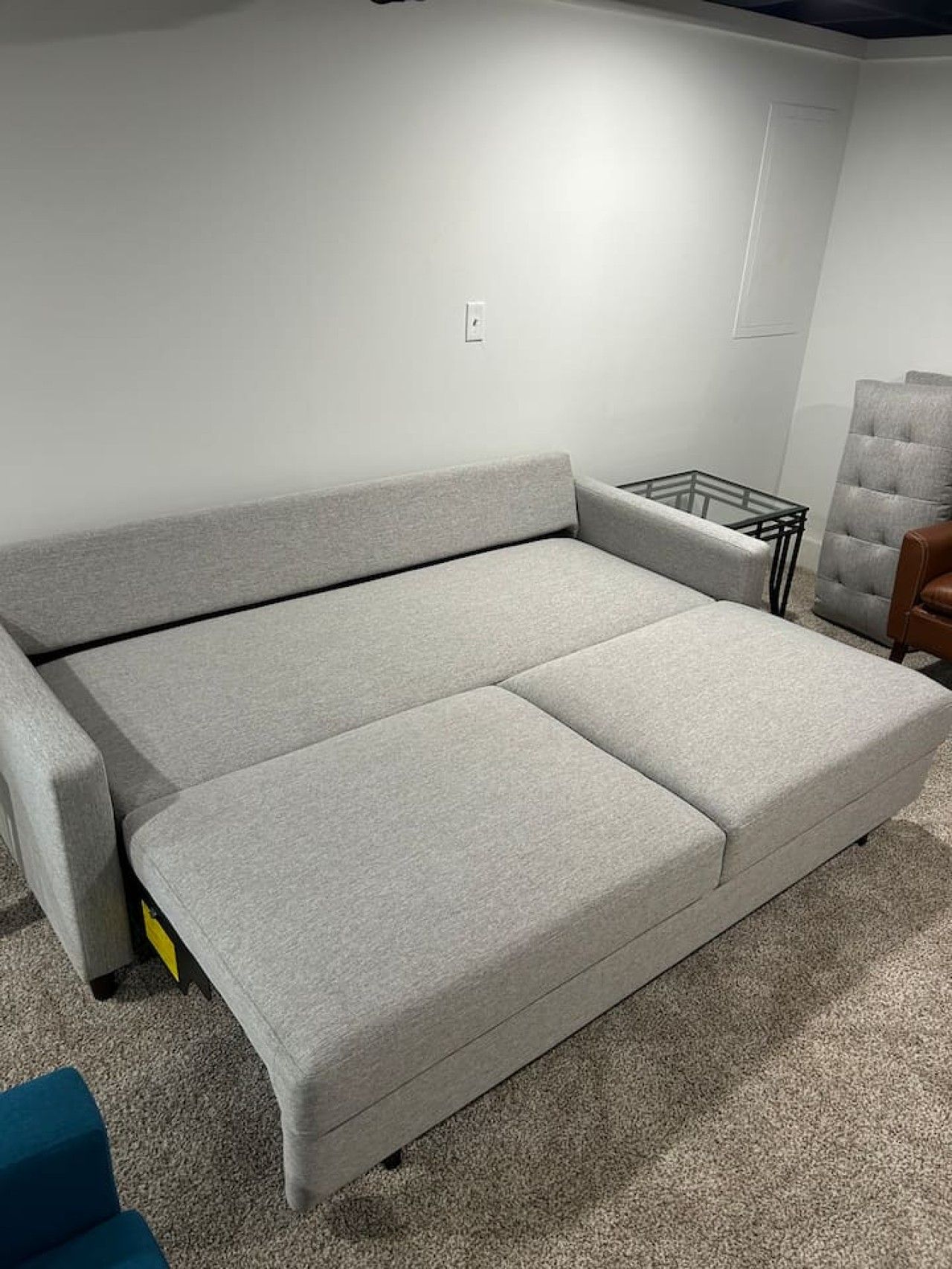 A grey sofa with a glass coffee table and a chair in a room with white walls.