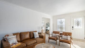 A living room with a brown leather sofa, two wooden chairs, a round coffee table, and a white door with windows.