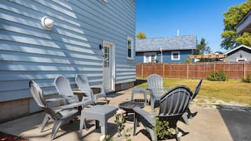 Een terras met tuinmeubilair, waaronder stoelen en een tafel, voor een huis met een blauwe gevel.