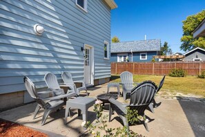 A patio with outdoor furniture, including chairs and a table, in front of a house with a blue siding exterior.