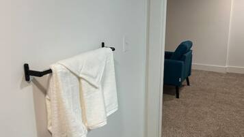 A room with a white wall, a black towel rack, a blue chair, and a carpeted floor.