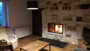 Een gezellige woonkamer met een stenen open haard, een comfortabele fauteuil, een salontafel en een televisie op een houten kast.